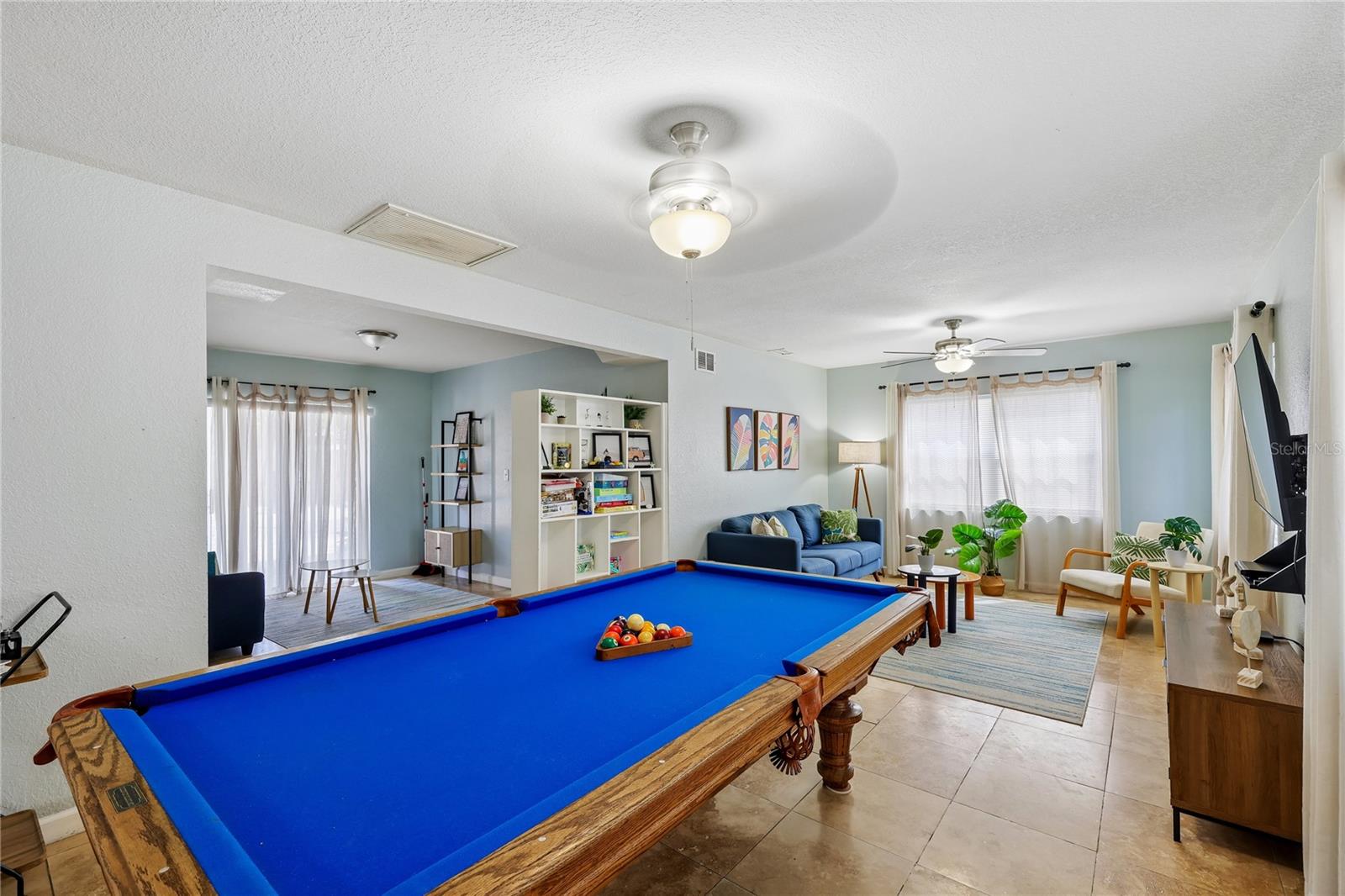 Game room with a large blue-felt pool table and a furnished living area behind it.