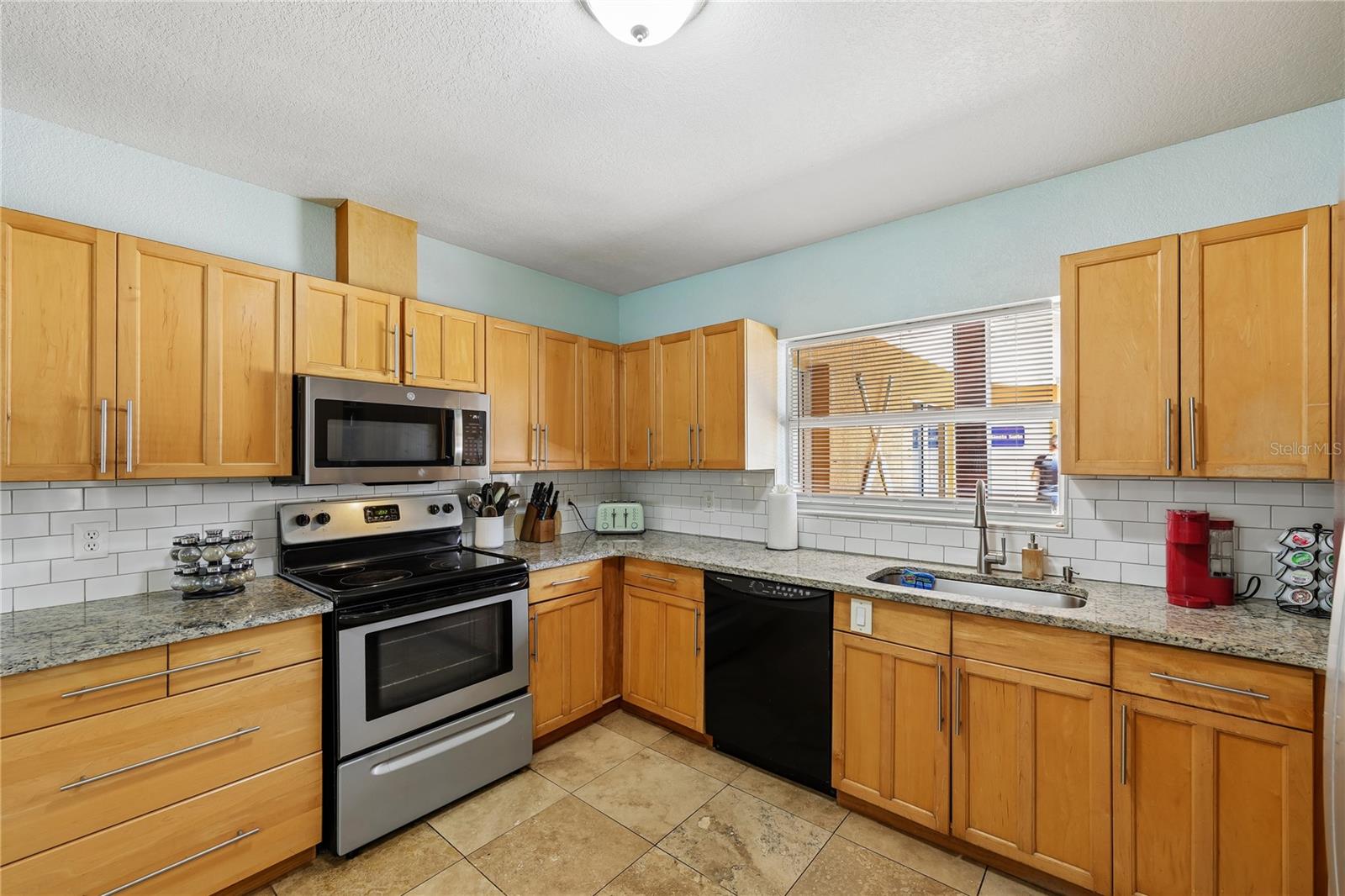 Kitchen with honey-colored cabinets, granite countertops, subway tile backsplash, and a window above the sink.