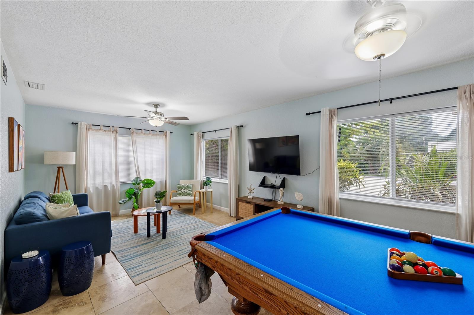Living room with a blue pool table, blue sofa, and large windows.