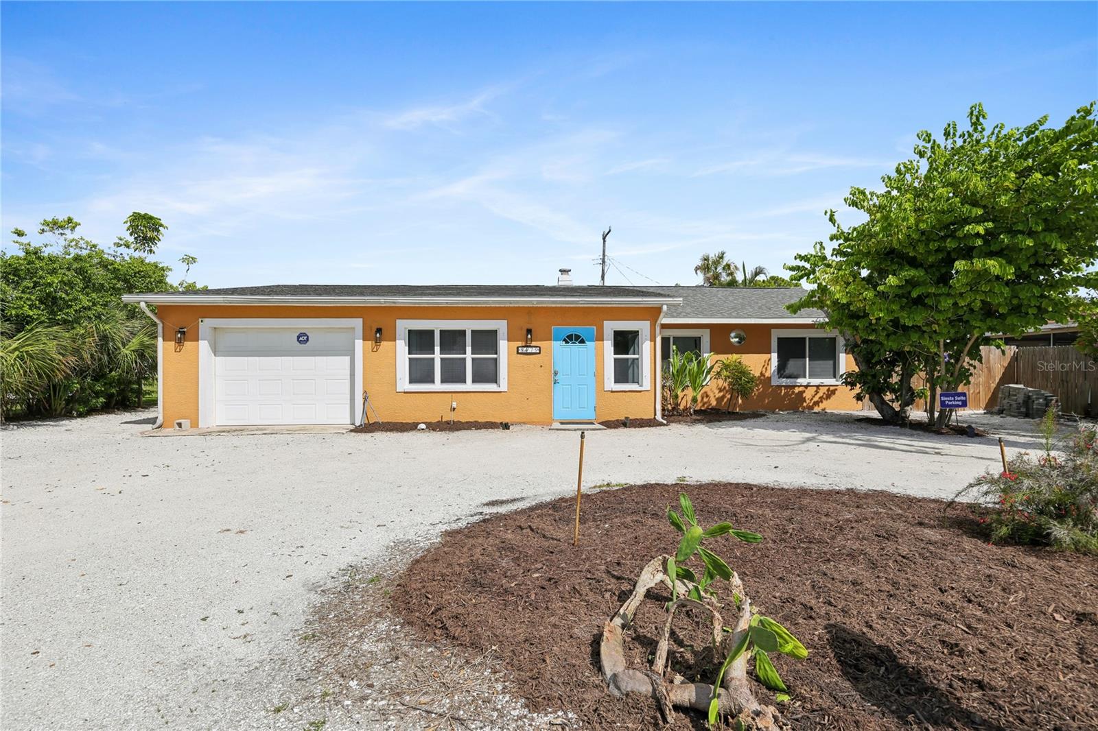 Orange single-story home with a bright blue front door, white garage, and gravel driveway.