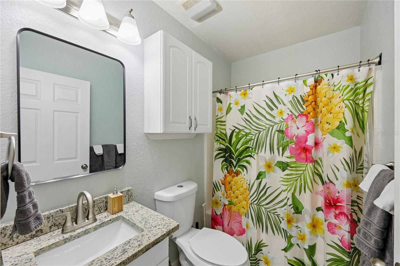 Bathroom with a granite vanity and colorful tropical floral shower curtain.