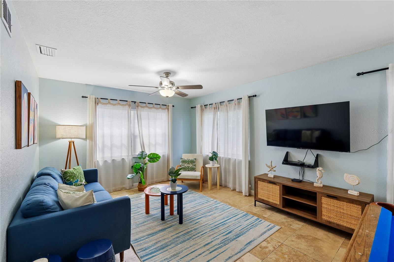 Furnished living room with a blue sofa, striped rug, and wall-mounted television.