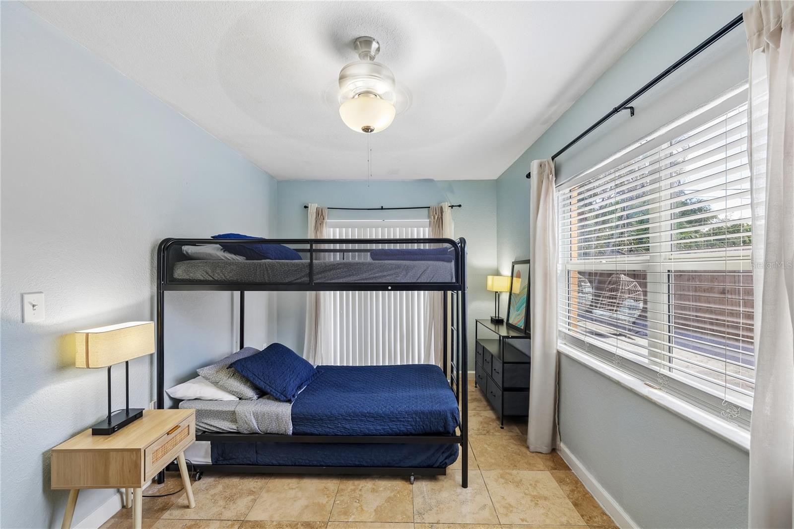 Bedroom with a black metal bunk bed, blue bedding, pale blue walls, and tile flooring.