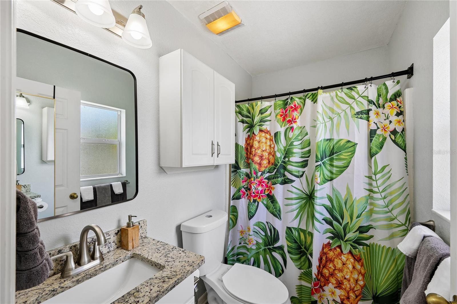 Bathroom with a granite vanity and a tropical-print shower curtain featuring pineapples and flowers.
