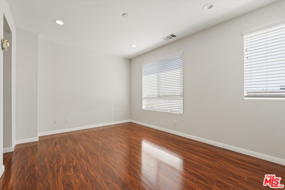 Empty room with polished hardwood floors and two windows with blinds.