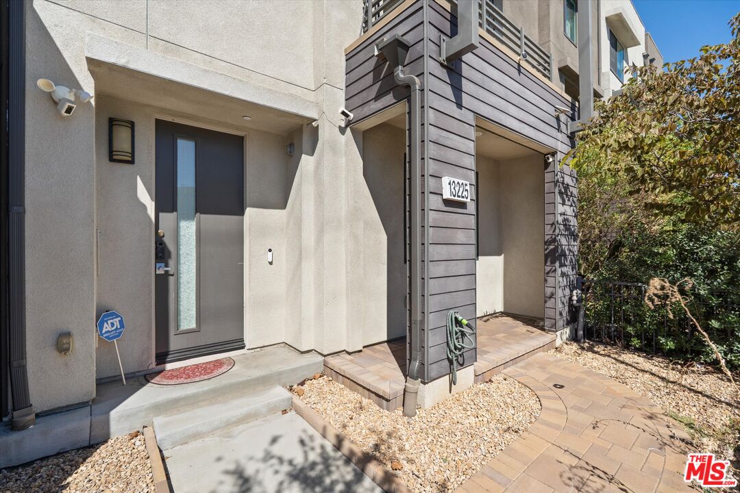 Entrance at 13225 Victory Blvd with a recessed front door, tiled porch, and curved paver walkway.