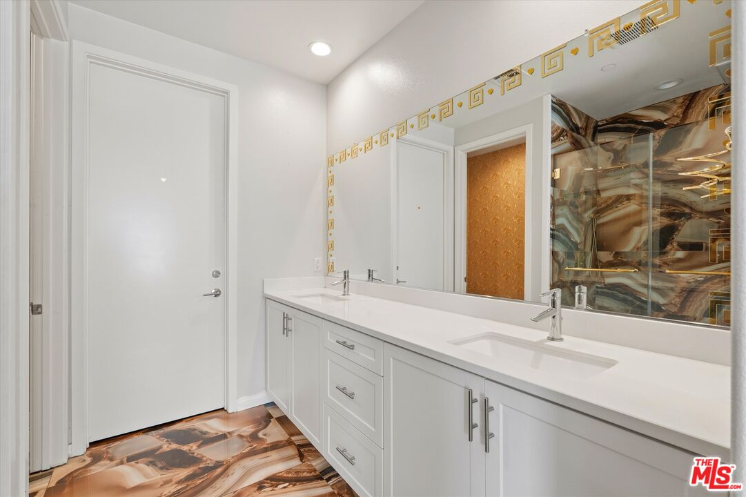 Bathroom with a white double-sink vanity, gold-trimmed mirror, and brown marbled tile.