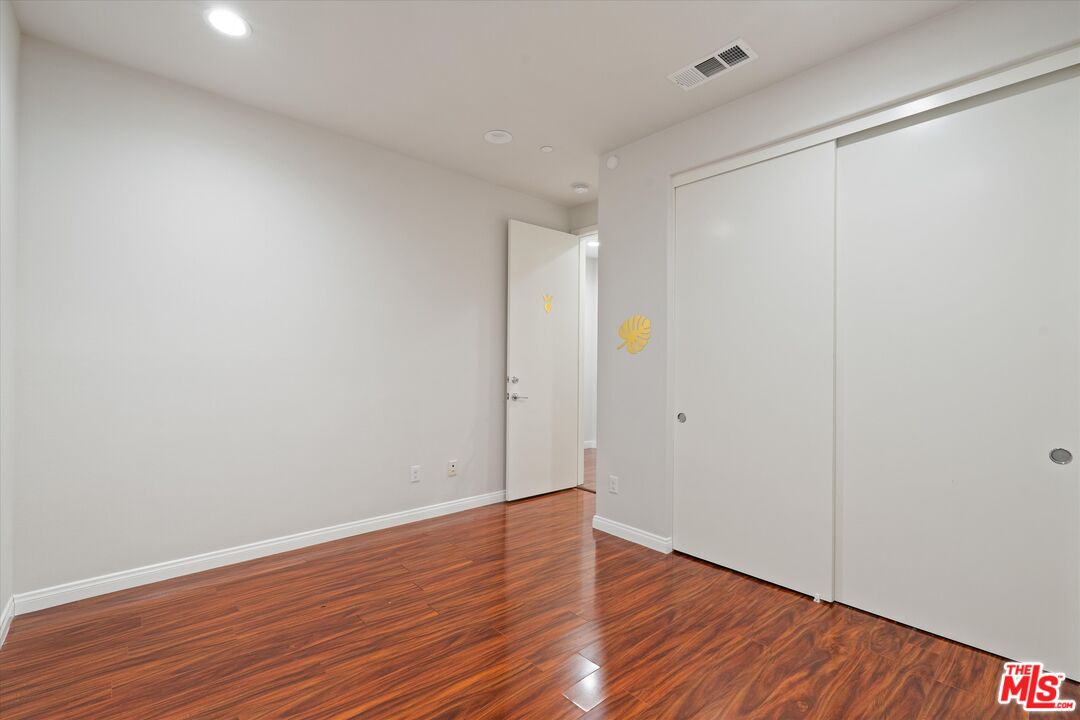 Empty room with reddish-brown hardwood floors, white walls, and a sliding-door closet.
