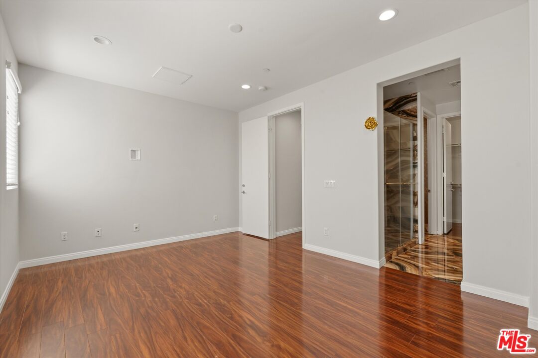 Empty room with glossy wood floors and an adjoining marble-floored area.