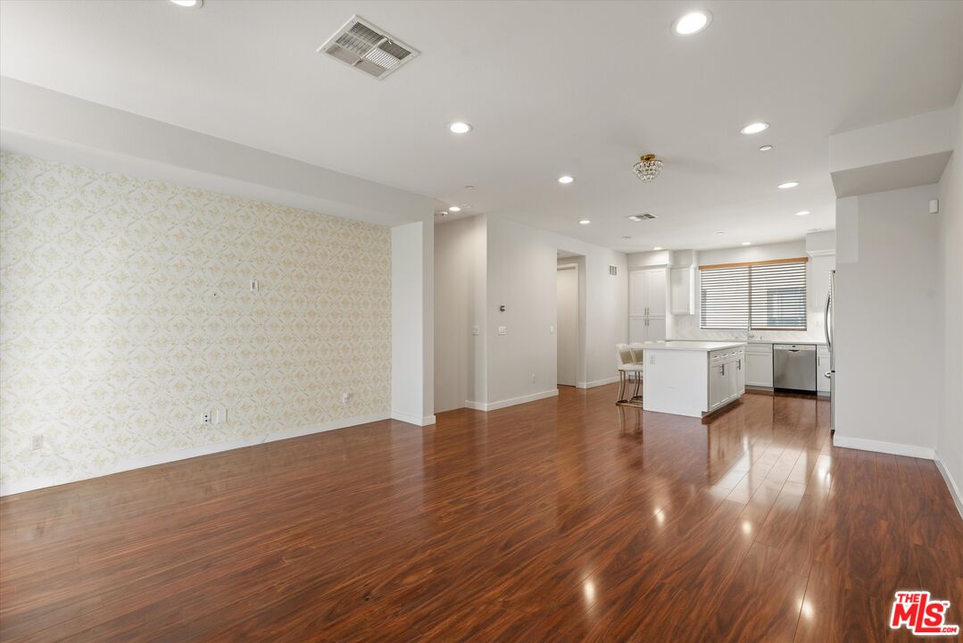Open living room and kitchen with polished wood floors, patterned accent wall, and a white island.