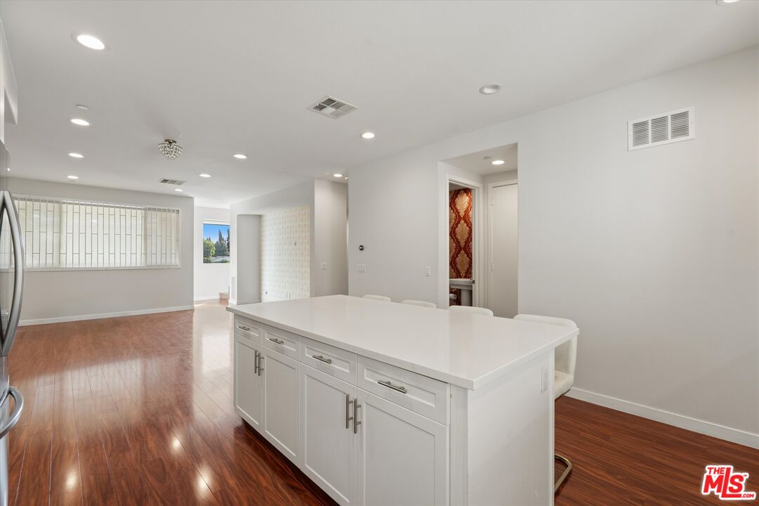 Open-plan kitchen with a large white island, white cabinets, and reddish-brown hardwood floors.