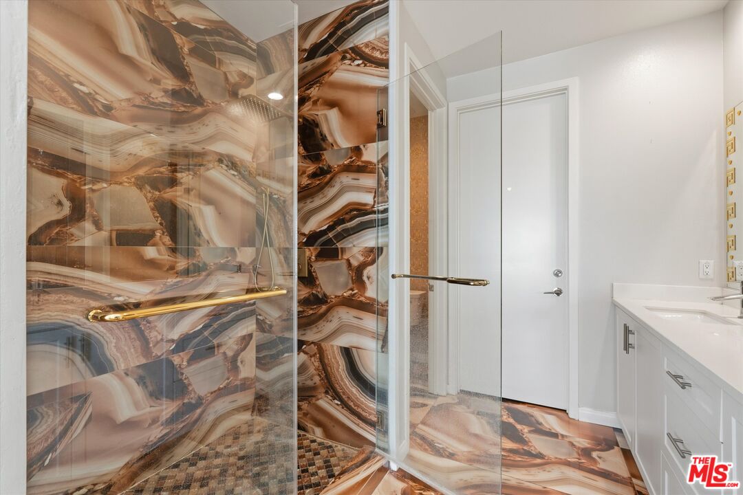 Bathroom with a glass shower lined in dramatic marble-patterned tile beside a white vanity.