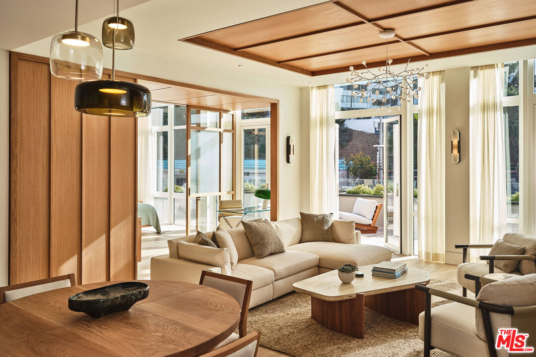 Contemporary living room with a cream sectional, wood dining table, and floor-to-ceiling windows.