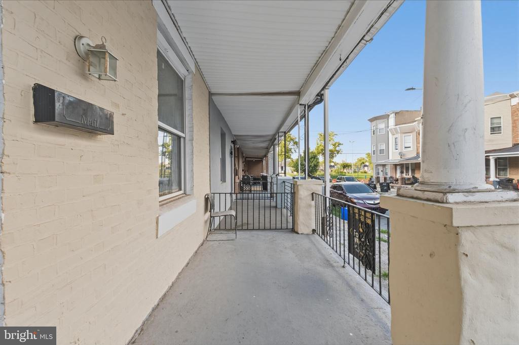 Covered front porch with white columns, black railings, and a view of the street.