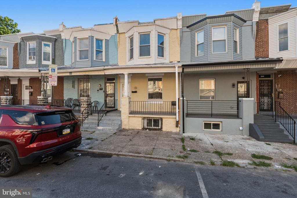 Philadelphia rowhouse with a covered porch, front steps, and a red SUV parked nearby.