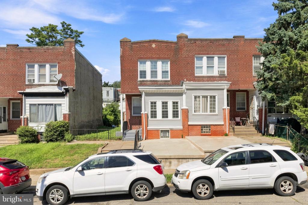 Red-brick attached home with a gray-sided front addition and concrete parking pads.