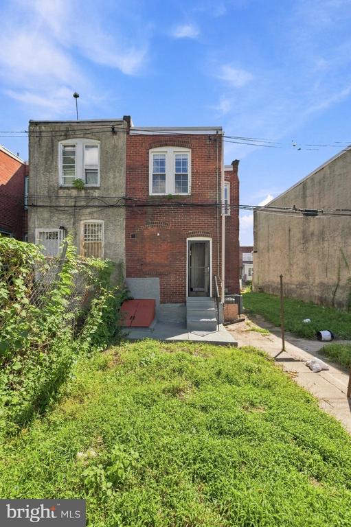 Attached brick house with a grassy yard, concrete entry steps, and neighboring buildings.
