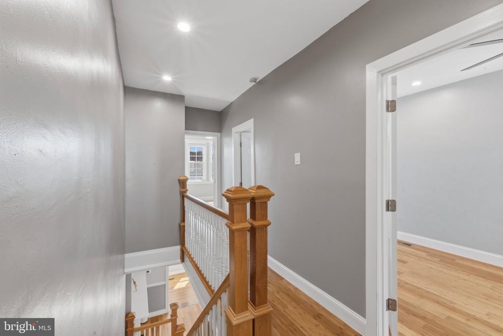 Upstairs hallway with hardwood floors, a wooden staircase railing, and an open doorway.