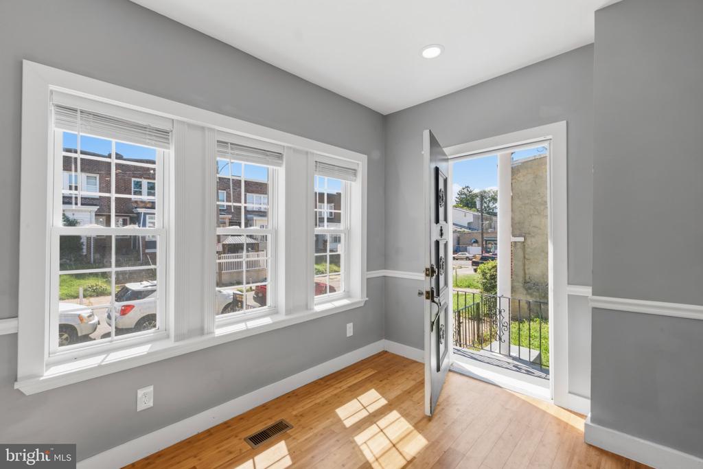 Vacant front room with gray walls, three windows, hardwood floors, and an open door to the porch.