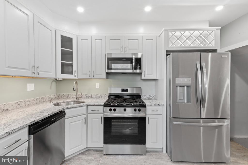 White kitchen with granite counters, stainless steel appliances, and a gas range.