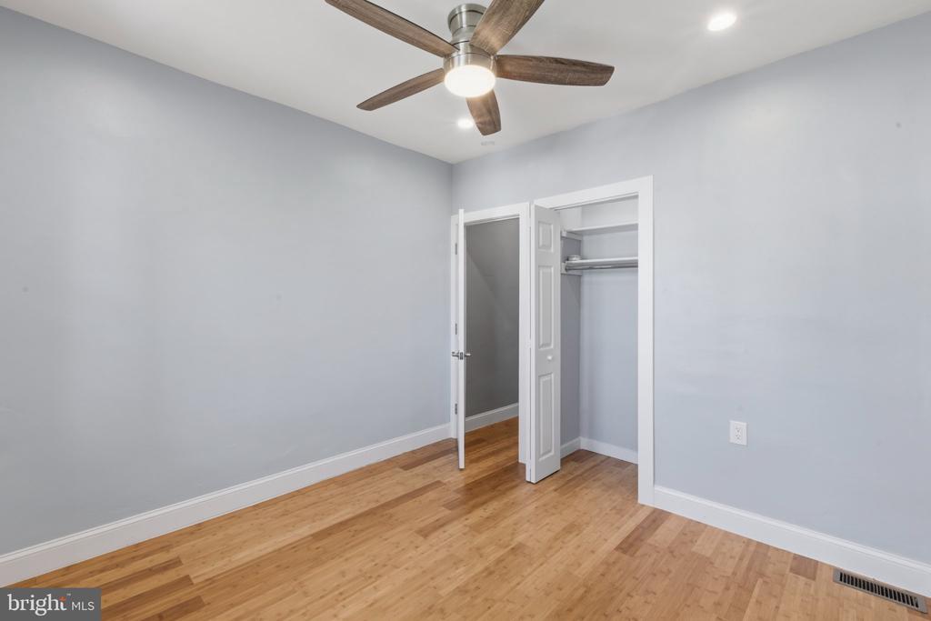 Empty bedroom with hardwood floors, an open closet, and a wood-blade ceiling fan.