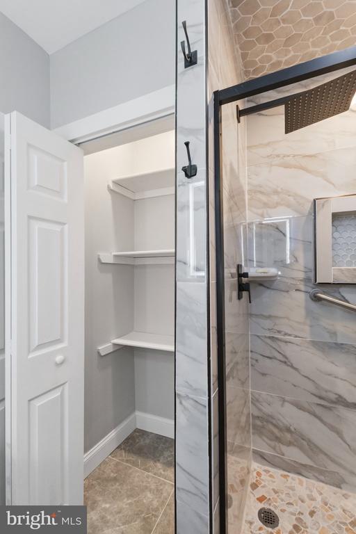 Bathroom with a glass walk-in shower and open linen closet shelves.