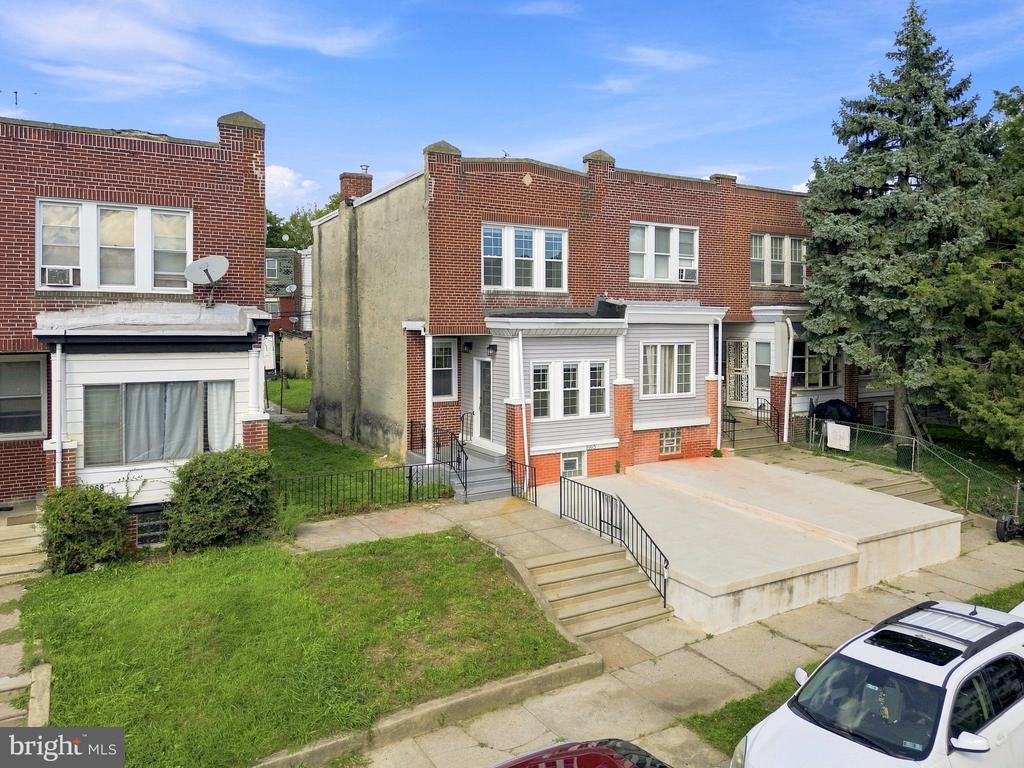 Brick rowhouse with a white-sided front addition, raised patio, and driveway.