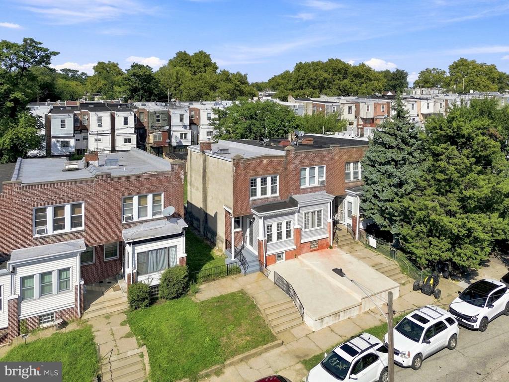 Aerial view of Philadelphia rowhouses with front steps, parked cars, and leafy trees.