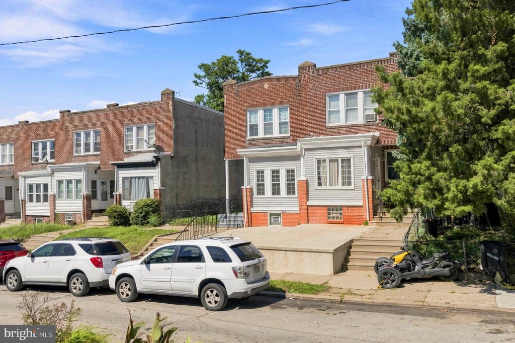 Red-brick rowhouse with gray siding and a raised concrete front area beside neighboring homes.