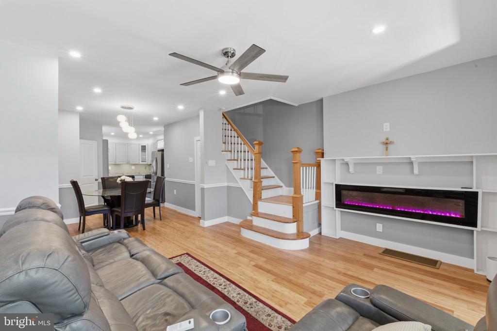 Living room with gray leather seating, an electric fireplace, hardwood floors, and an open staircase.