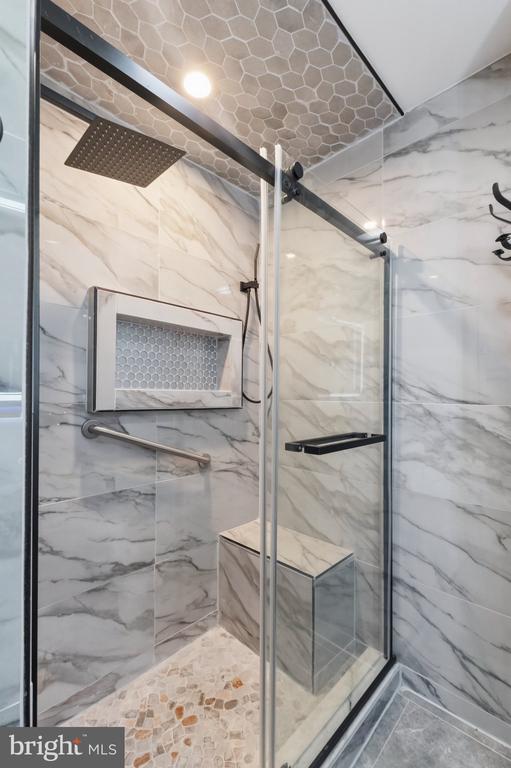 Walk-in shower with marble-look tile, a glass enclosure, rainfall showerhead, and built-in corner bench.