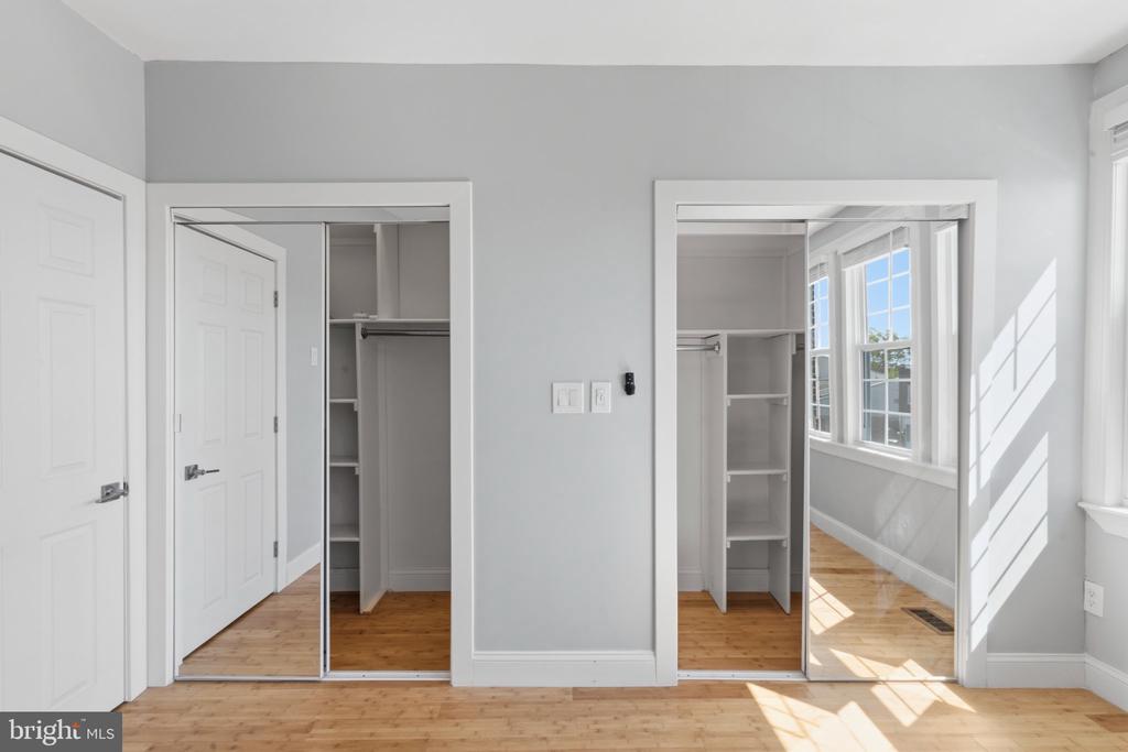 Bright vacant room with hardwood floors, open closets, and sunlight from adjoining windows.