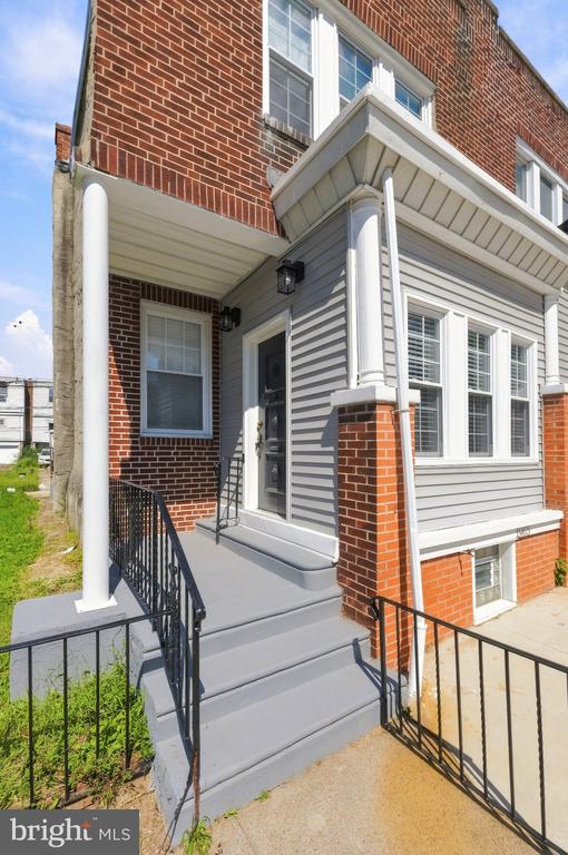 Red-brick house with gray siding, a covered entrance, broad steps, and black railings.