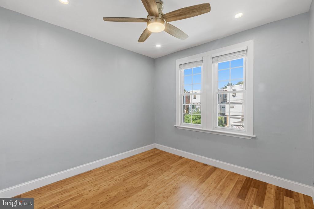 Empty bedroom with hardwood floors, two windows, and a wood-blade ceiling fan.