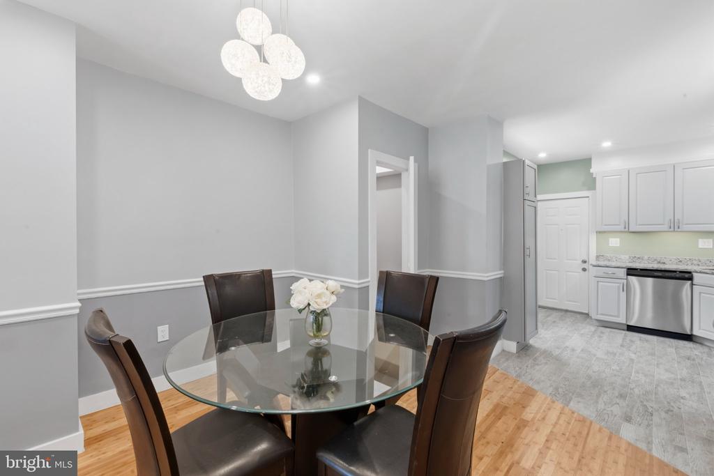 Dining room with a glass table, dark leather chairs, and an adjoining white kitchen.
