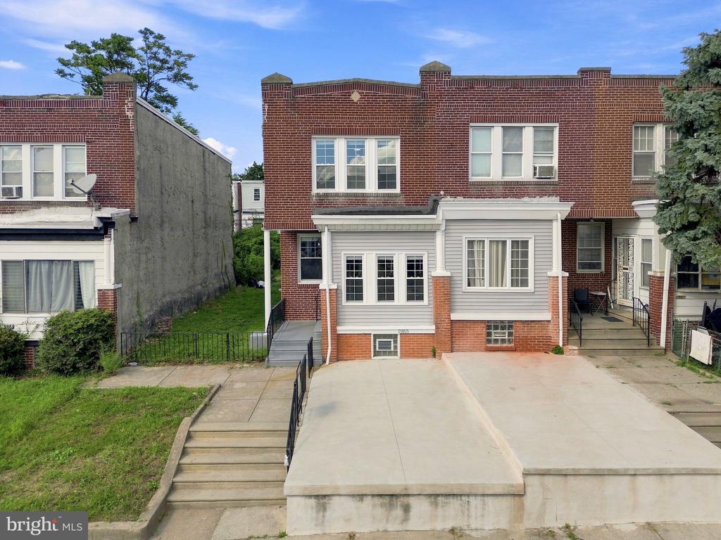 Red-brick row house with white lower facade and a raised concrete parking pad.