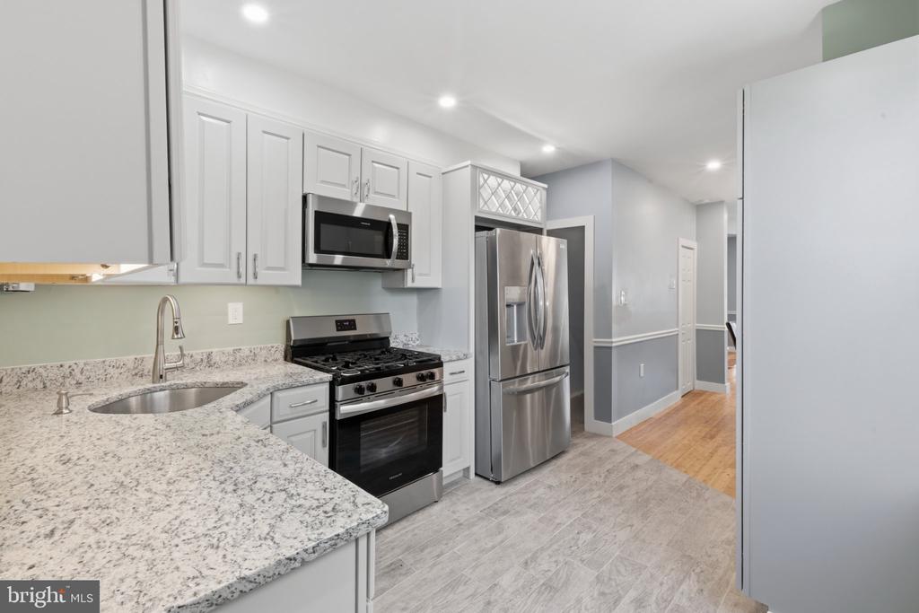 Kitchen with white cabinetry, stone countertops, stainless steel appliances, and gray tile flooring.