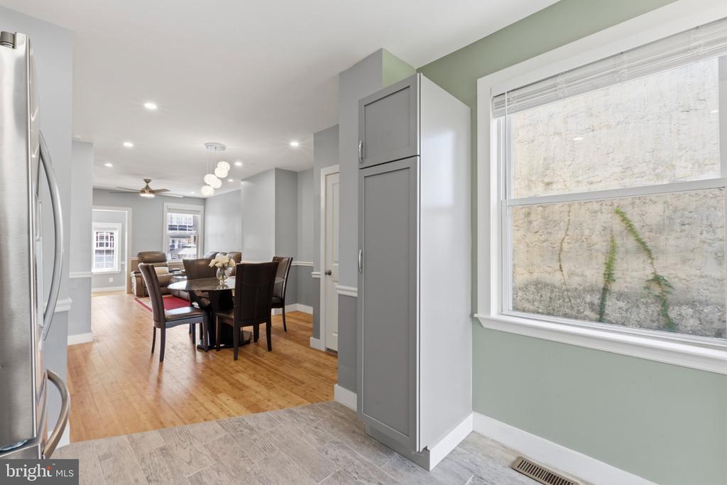 Kitchen opening to a dining area, with tall gray cabinets, a large window, and hardwood floors.