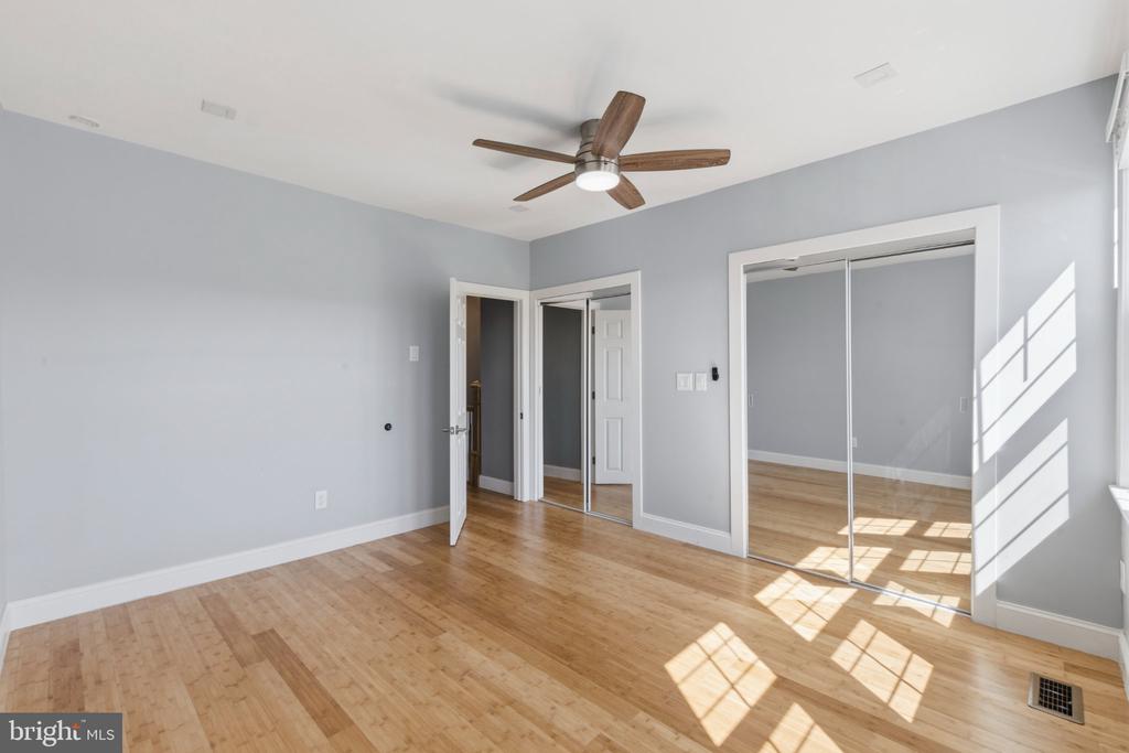 Empty bedroom with hardwood floors, a ceiling fan, and mirrored sliding closet doors.