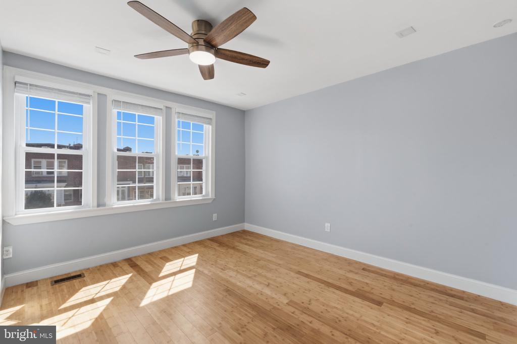 Empty bedroom with three windows, hardwood floors, and a wood-blade ceiling fan.