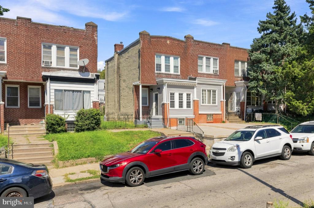 Red-brick Philadelphia row house with a white enclosed porch and small front lawn.