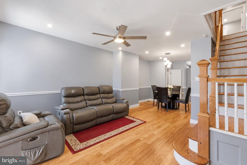 Living and dining area with gray reclining sofas, a red rug, hardwood floors, and a wooden staircase.