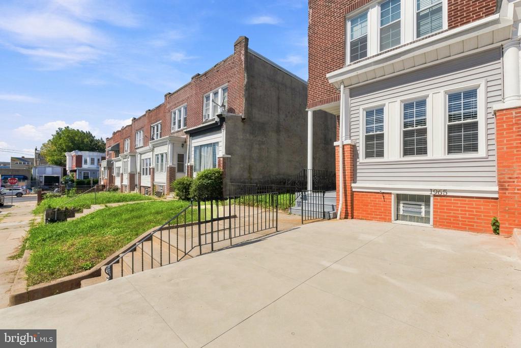 Philadelphia rowhouse with brick and light siding, front windows, and a fenced concrete walkway.