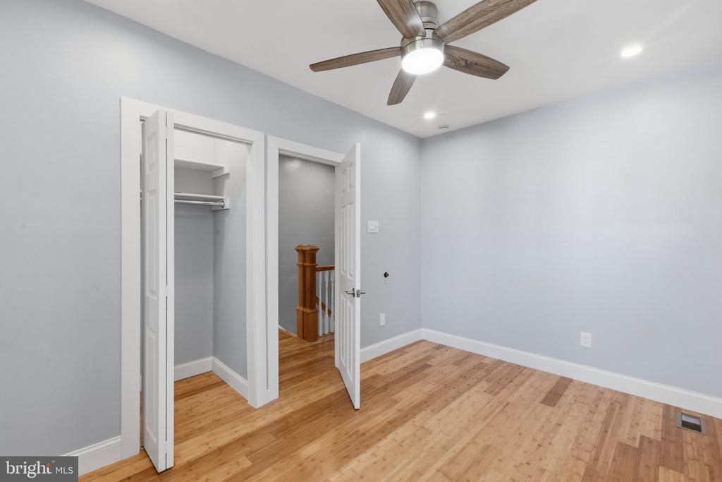 Unfurnished room with hardwood floors, ceiling fan, and open closet beside a stairway.