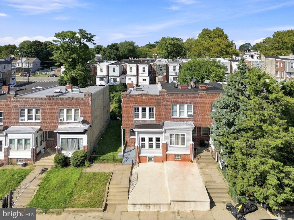 Rear aerial view of a red-brick rowhouse with a wide concrete parking pad and mature trees.