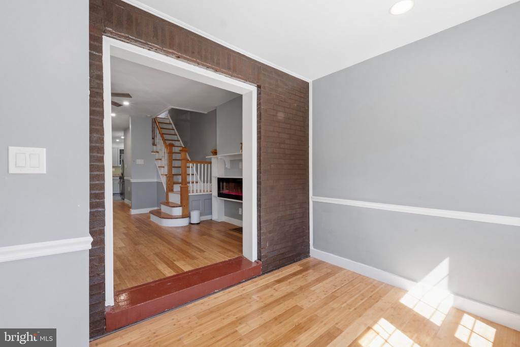 Vacant room with hardwood floors and gray walls, looking through a brick opening toward a staircase and fireplace.