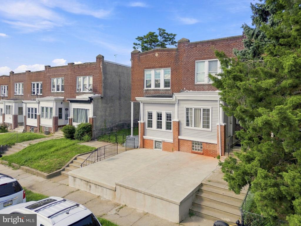 Brick rowhouse with a white-sided front addition, raised concrete patio, and neighboring attached homes.
