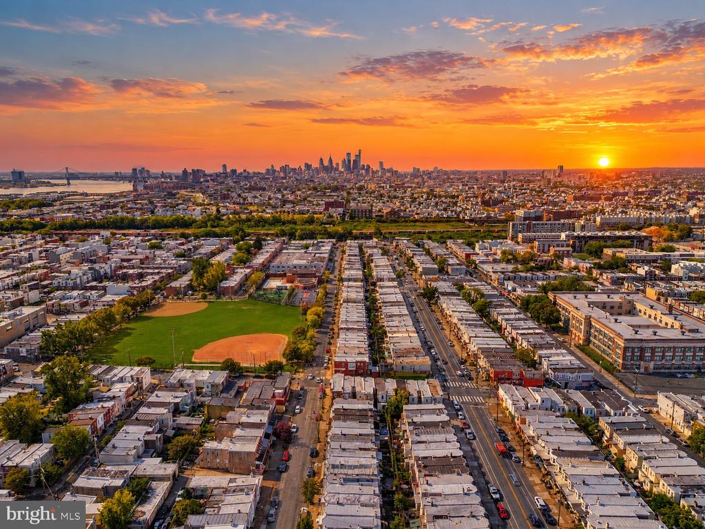 Aerial view of Philadelphia row houses and downtown skyline at sunset, with a baseball field in the foreground.