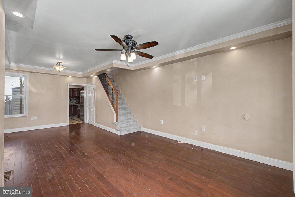 Vacant living room with dark hardwood floors and a staircase with carpeted steps.