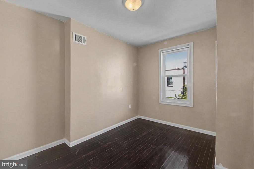 Empty room with beige walls, dark hardwood floors, and a single window.
